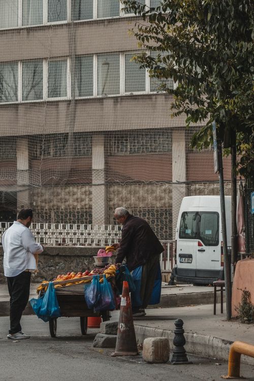 Free Street vendor selling fruits from a cart in an urban area with nearby commercial buildings. Stock Photo