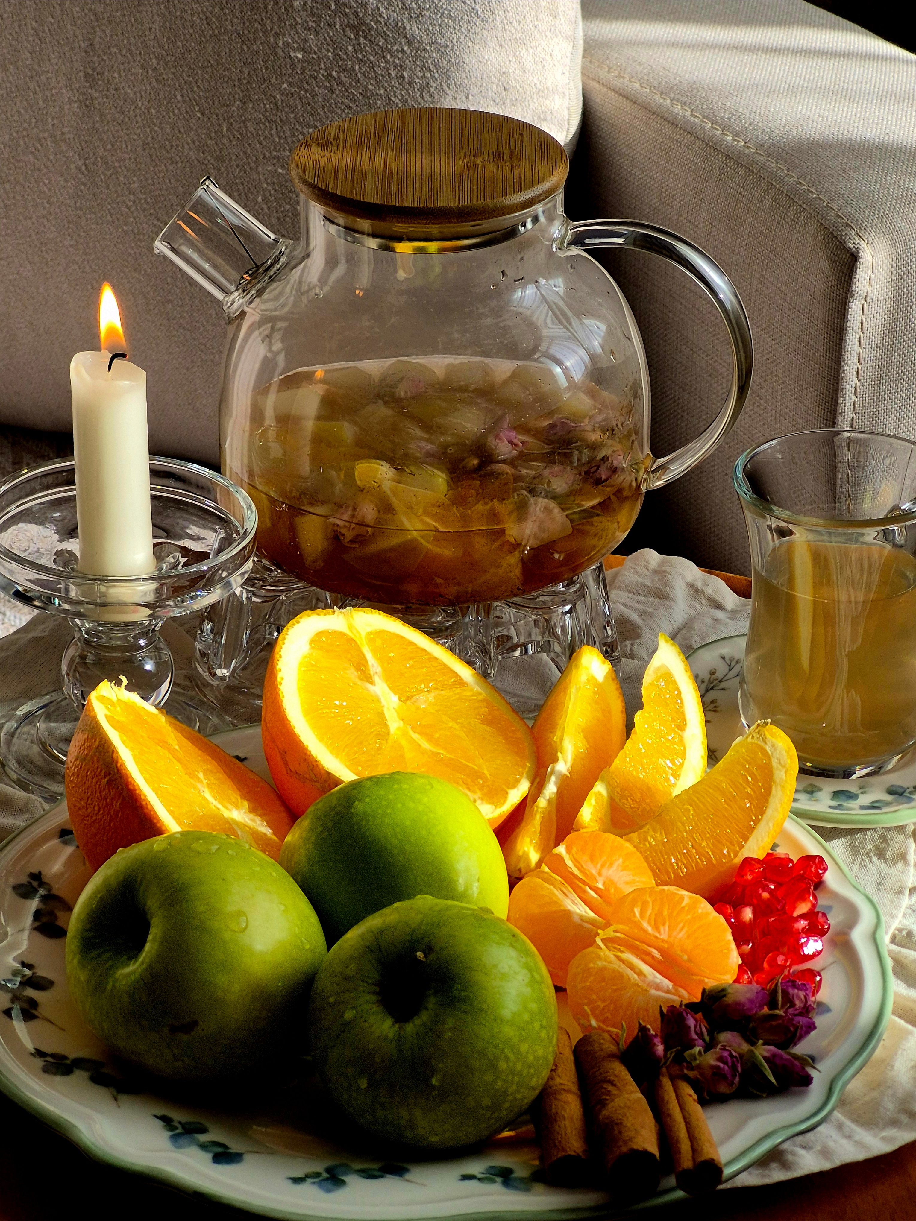 Inviting tea scene with fresh oranges, apples, and candlelight for a cozy ambiance.