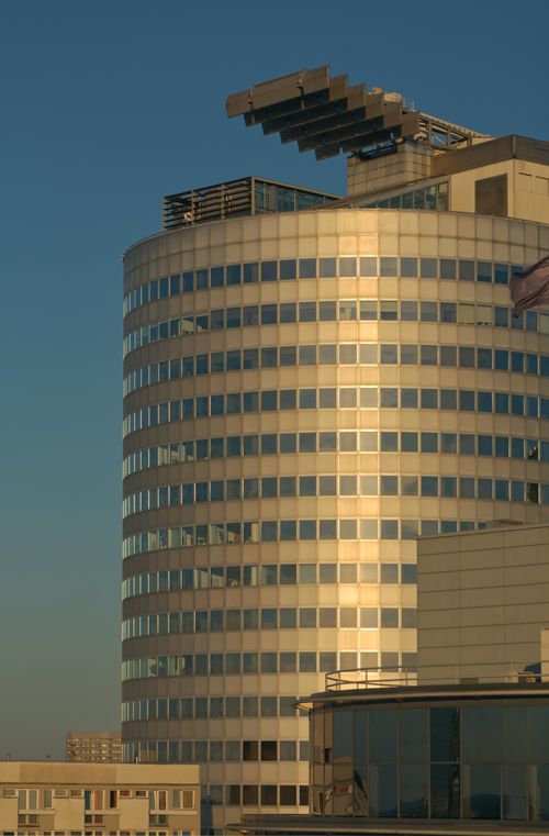 Free A modern circular office building reflecting sunset light, featuring unique rooftop structures. Stock Photo