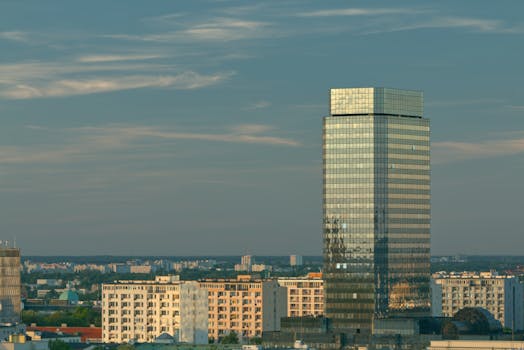 A towering glass skyscraper amidst a cityscape, reflecting the clear blue sky.