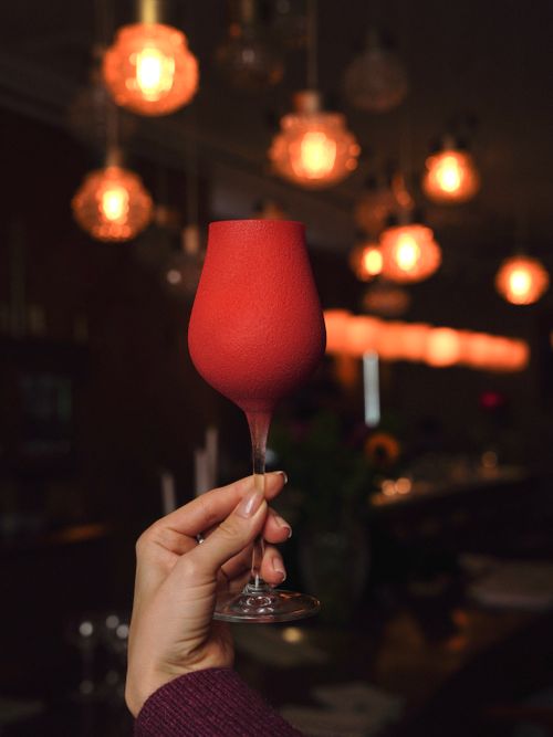 Free Red wine glass held up in a stylish bar with soft warm lighting, creating a cozy ambiance. Stock Photo