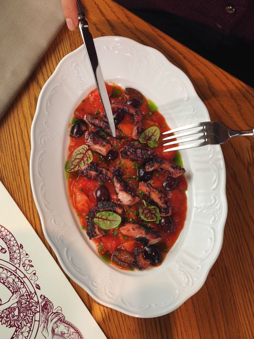 Free Elegant grilled octopus dish with tomato and olives on a wooden table setting. Stock Photo