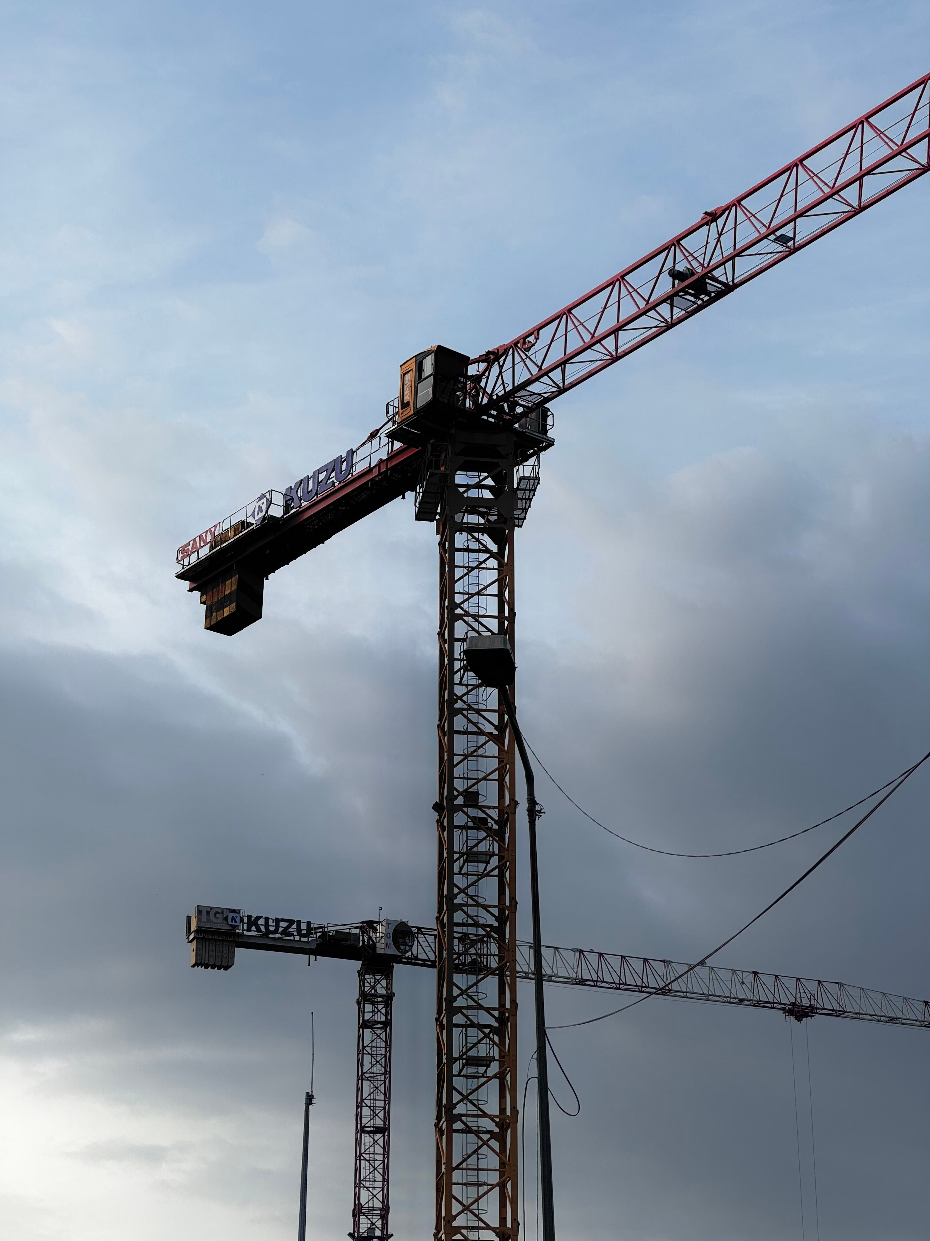 Two tower cranes in construction site silhouetted against a cloudy sky.