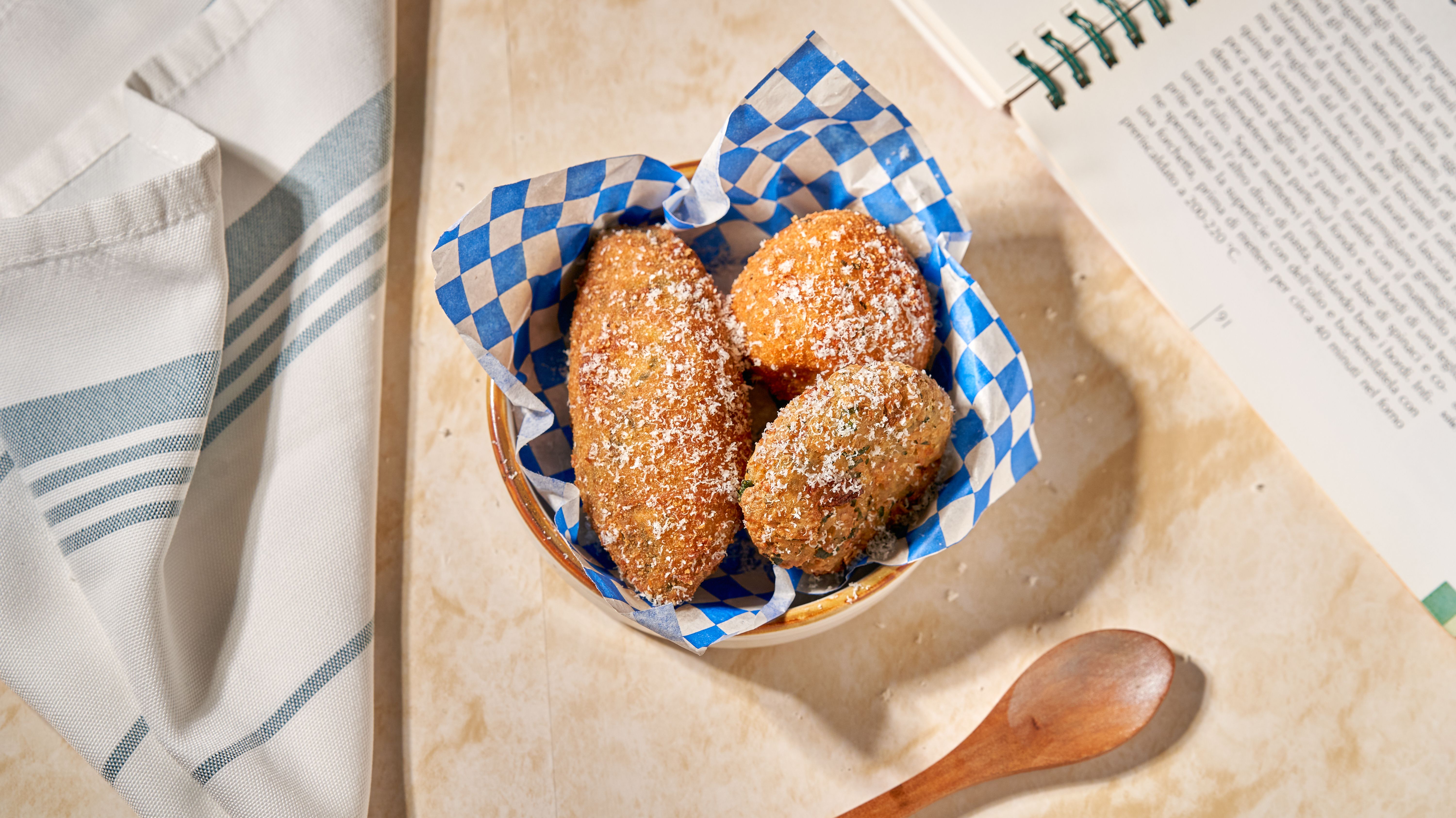 Tasty fried croquettes in a checkered paper-lined basket with a cookbook.