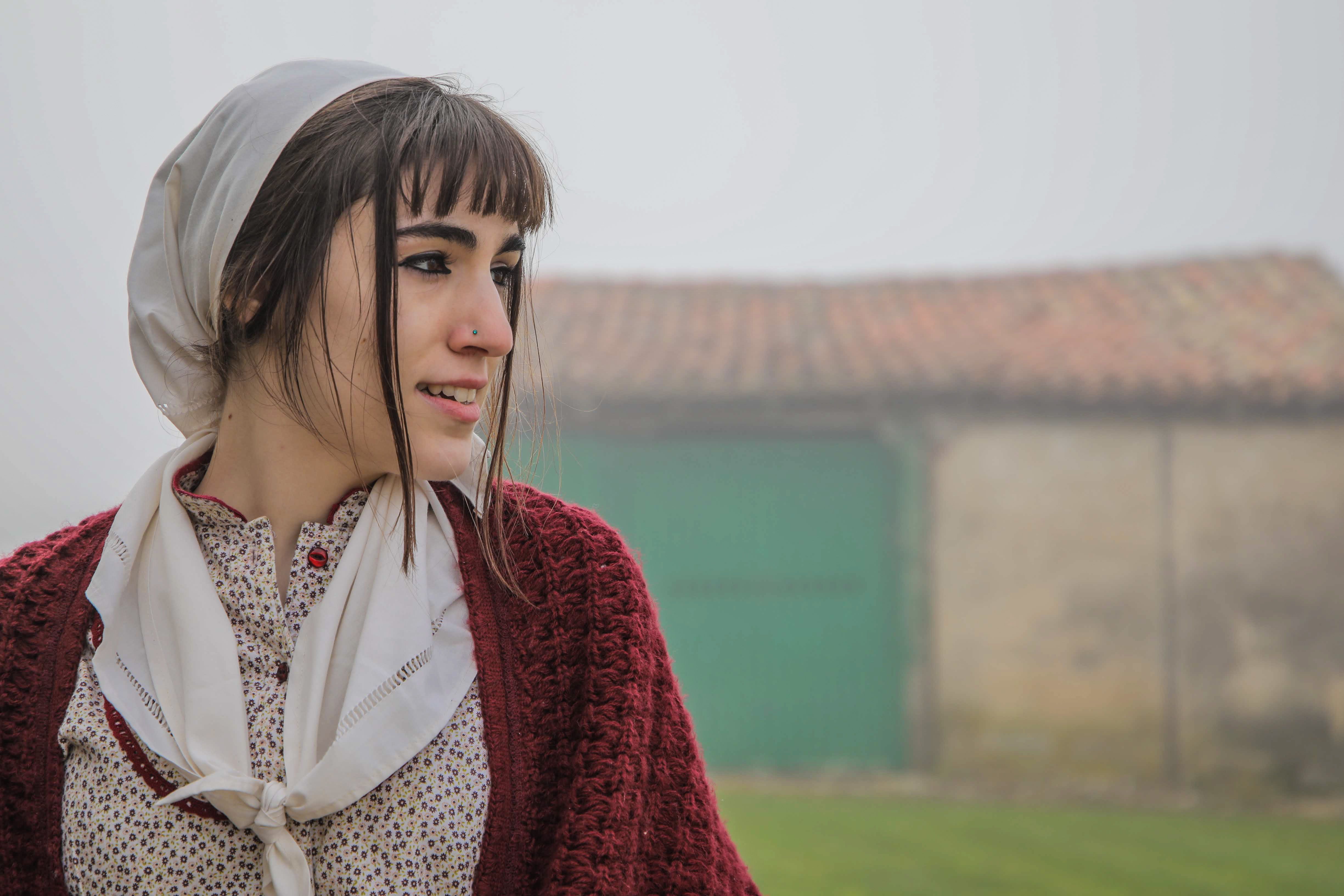Portrait of a young woman wearing a headscarf, standing outdoors on a foggy day.