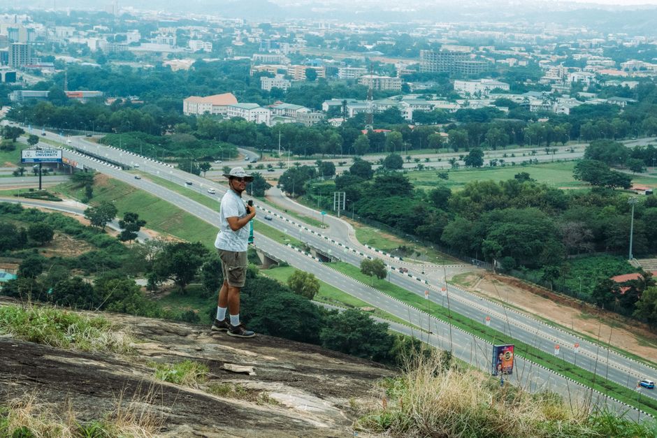 A hiker stands on a hill overlooking a sprawling cityscape under a cloudy sky.
