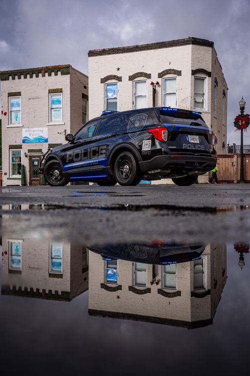 Free Urban scene featuring a police vehicle reflecting in a puddle near historic buildings. Stock Photo