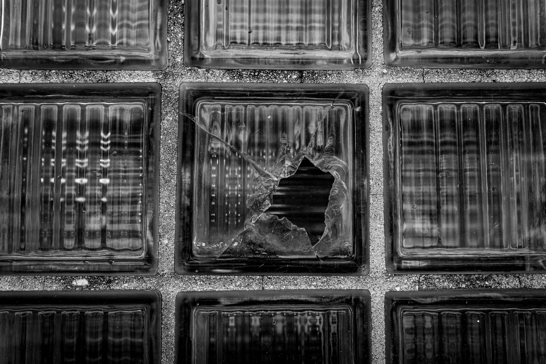 A black and white photo of a cracked glass block in an industrial setting, offering artistic texture.