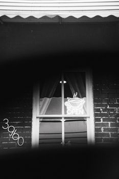 Moody black and white photo of a cafe window featuring a steaming cup neon sign.