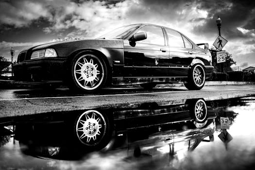 Black and white photo of a car with dramatic reflections on wet pavement.