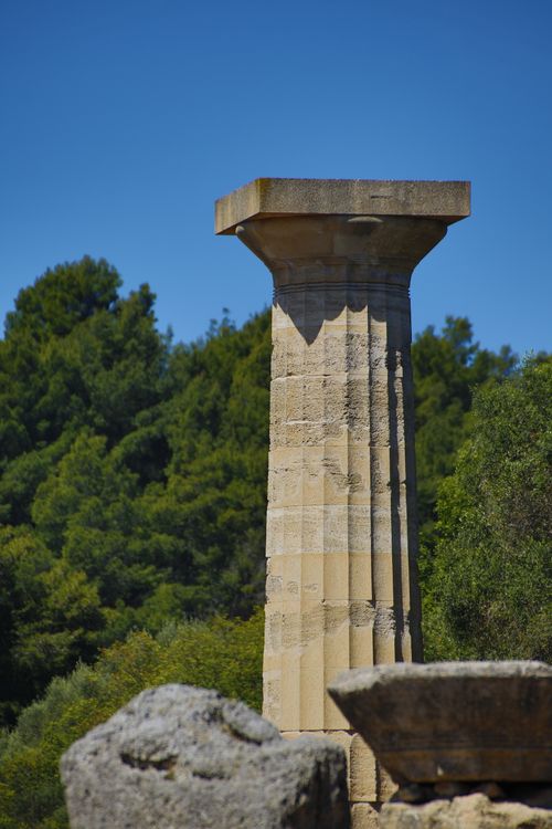 Free Ancient Doric column remains amidst lush greenery under a clear blue sky. Stock Photo