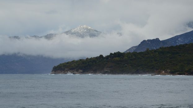 Dramatic view of a mountain and rugged coastline in Saint-Florent, Corsica, with misty clouds.