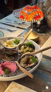 Delicious Middle Eastern appetizers including hummus and vine leaves under a vibrant mosaic lamp.