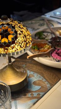 Close-up of a decorative Middle Eastern lamp beside a tray of vibrant mezze dishes on a wooden table.