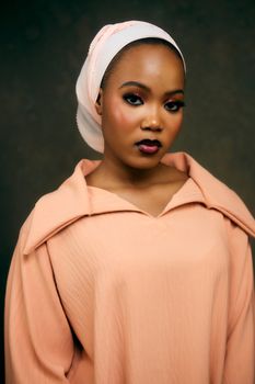 Stylish portrait of a woman in peach outfit with headscarf, showcasing elegance and beauty.