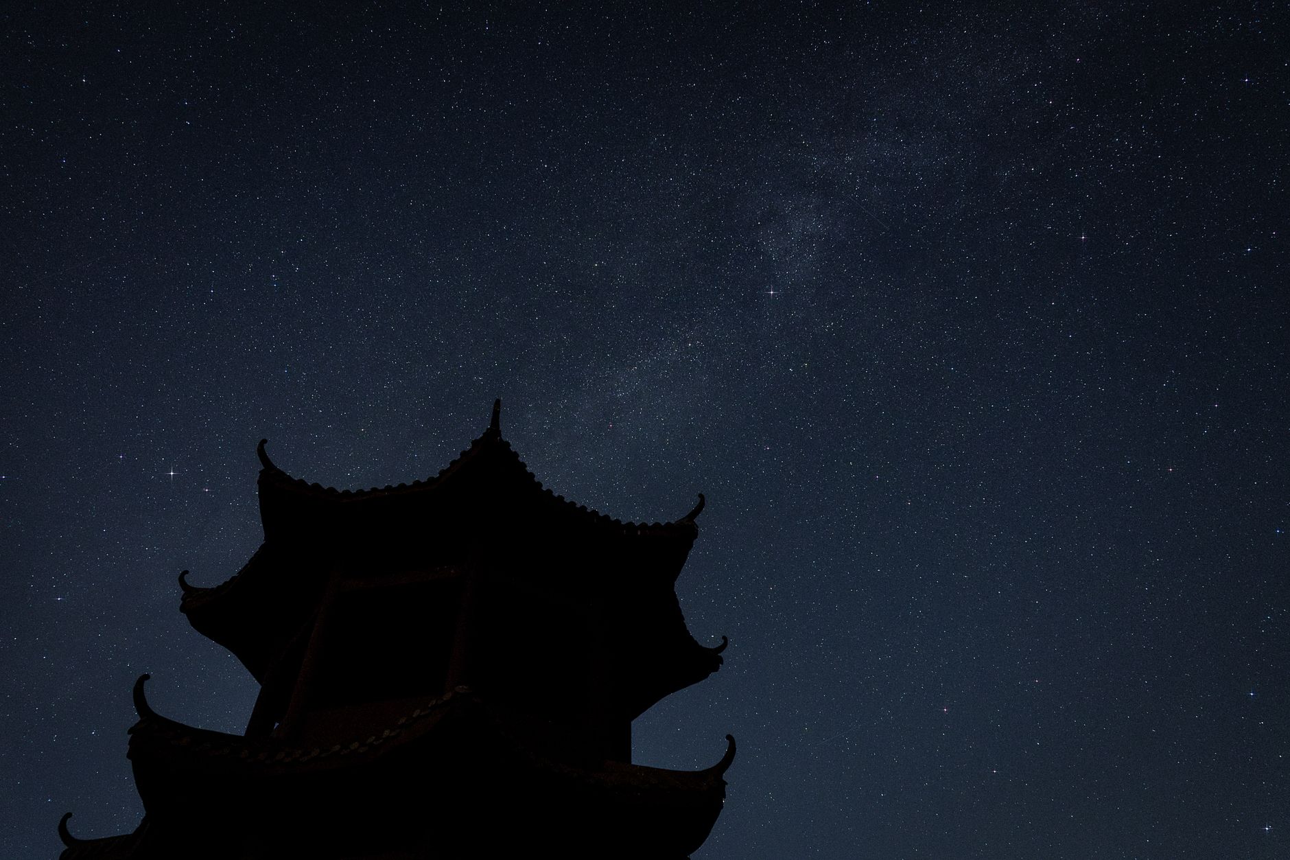 Silhouette of a traditional pagoda with a breathtaking starry night sky in the background, showcasing the Milky Way.