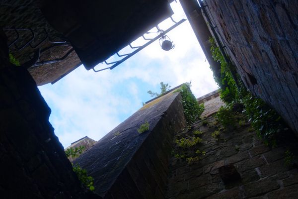 Contre-plongée entre de vieux murs de pierre avec lierre et lanterne suspendue