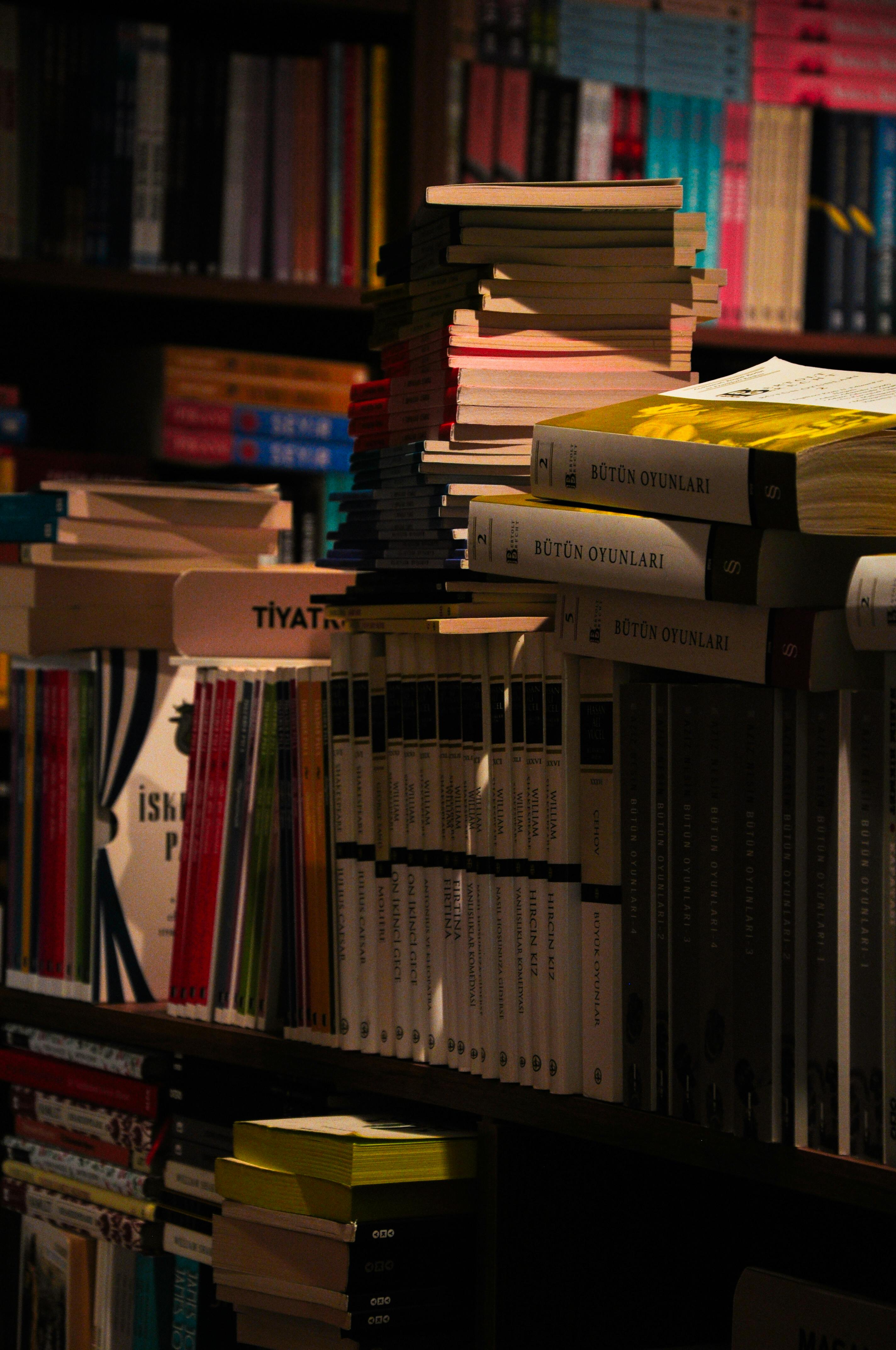 Gratuit Scenă de bibliotecă slab luminată, cu o varietate de cărți stivuite pe un raft. Fotografie de stoc