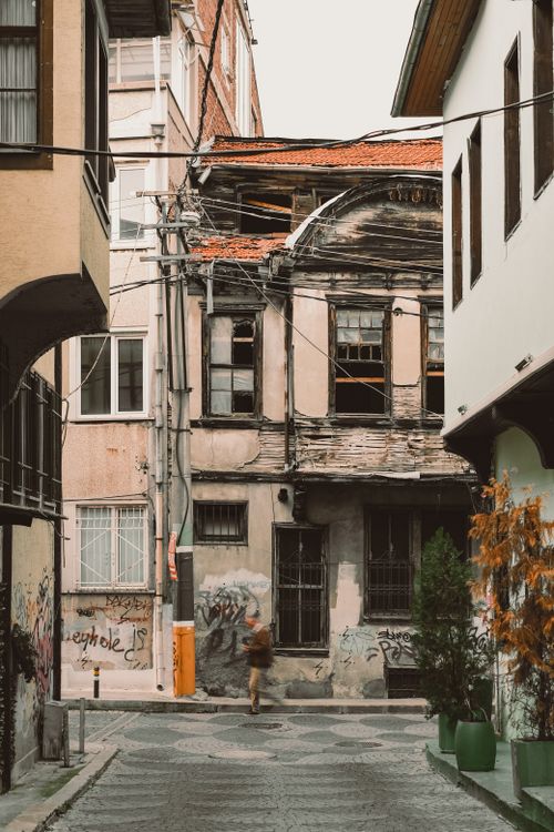 Free Person walking down a narrow alleyway with an old, weathered building facade in a cityscape. Stock Photo