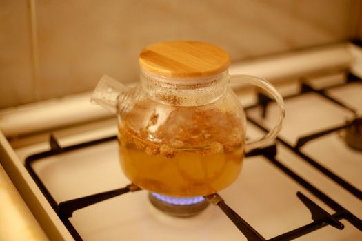 A glass teapot brewing herbal tea on a kitchen gas stove with a warm ambiance.