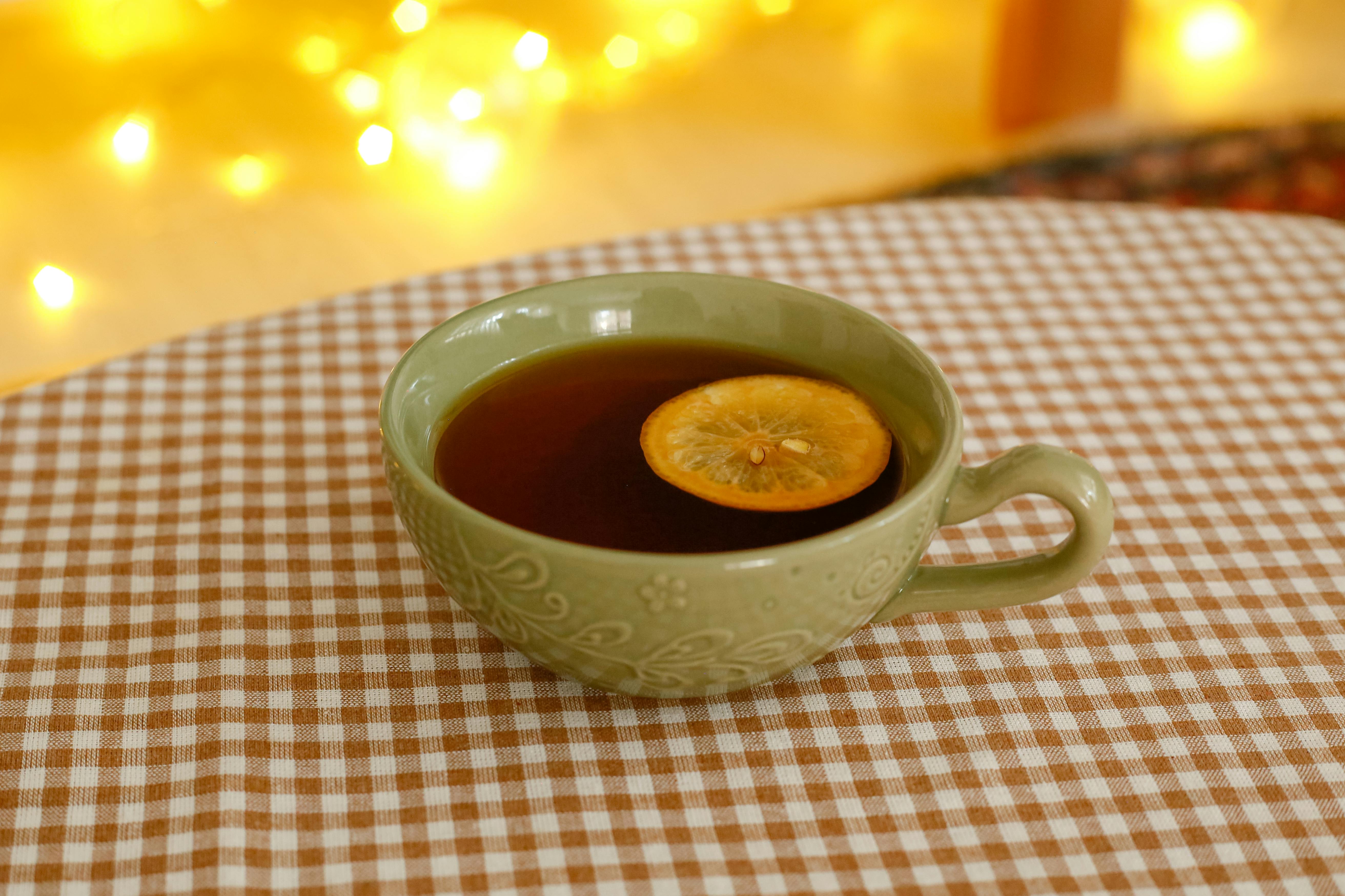 Warm cup of tea with lemon slice on checkered tablecloth, cozy ambiance.