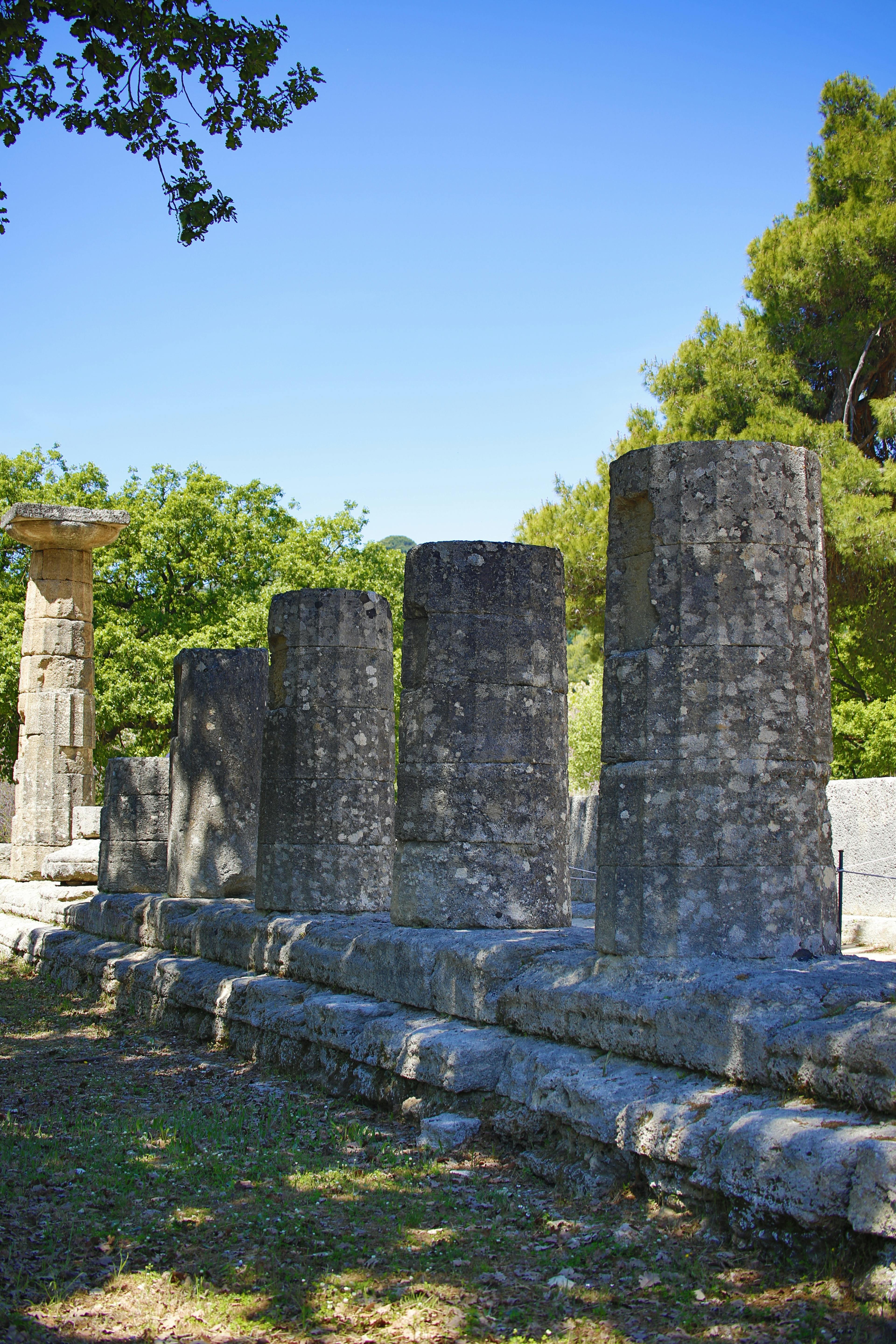 Ancient stone columns of Olympia's temple ruins under clear blue sky.