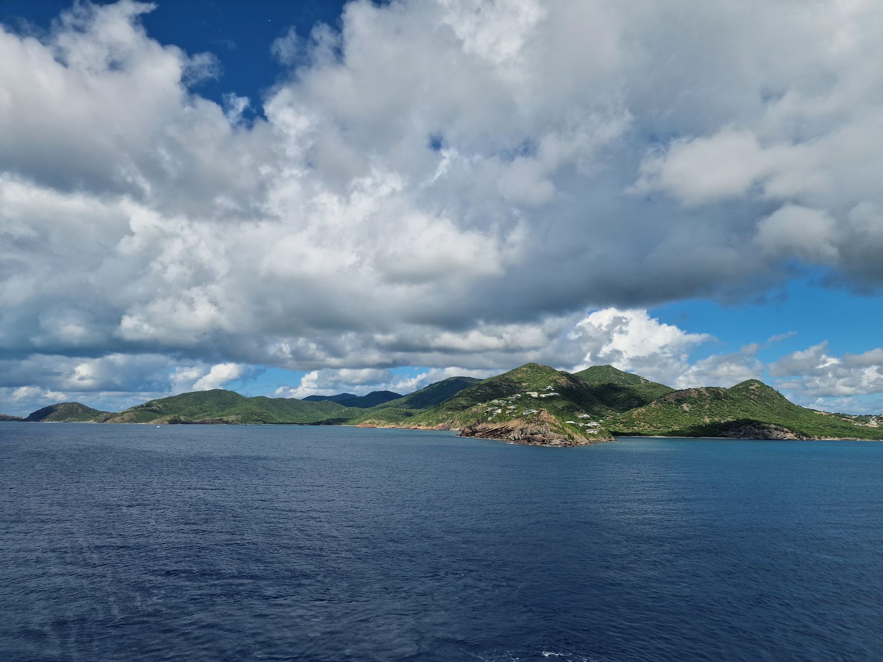 Beautiful Caribbean island with lush hills and a vast ocean under a bright sky.