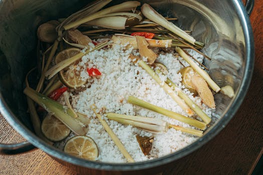 Top view of lemongrass, lime, ginger, and red chili with rice in a pot.