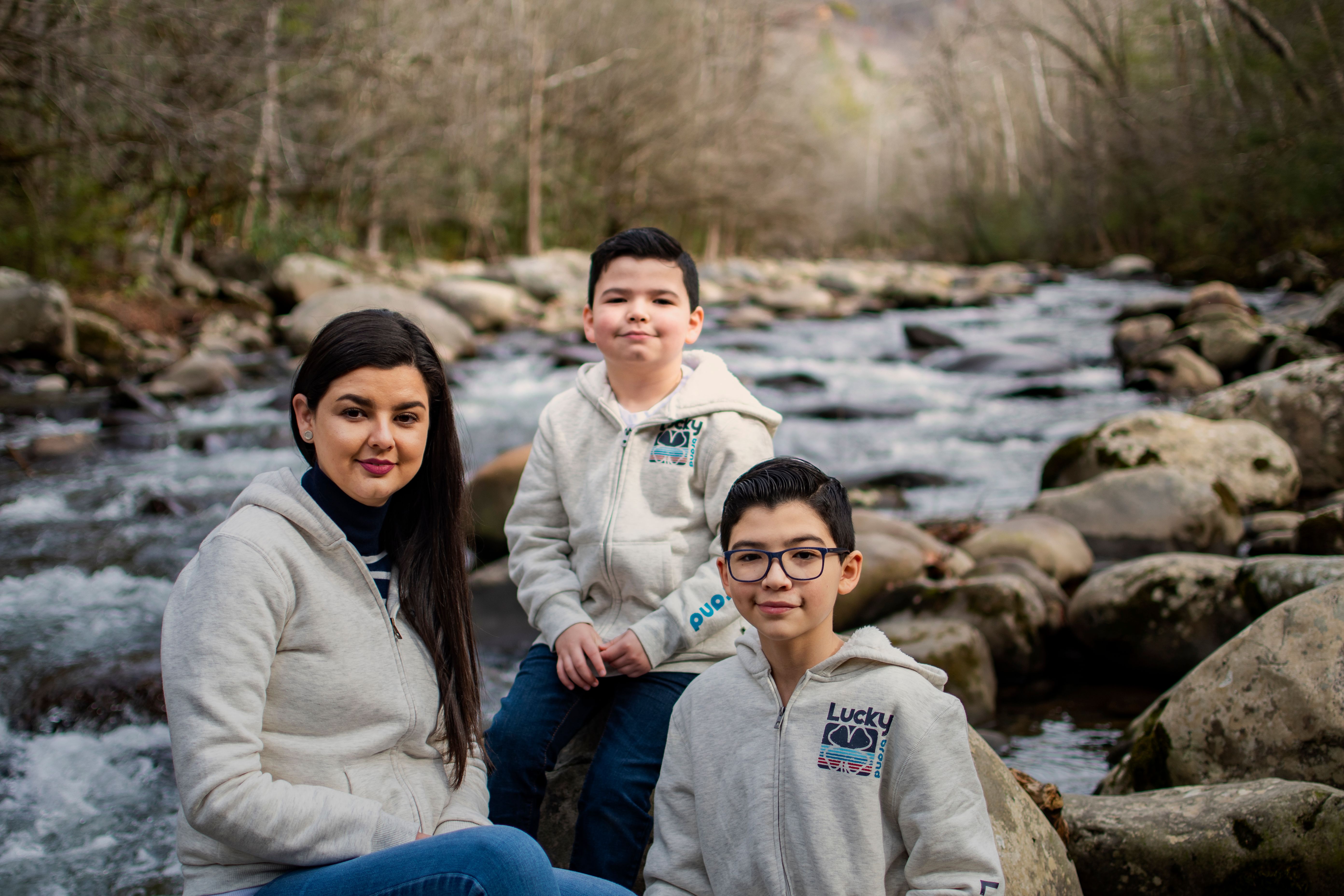 A family sits by a rocky river in a serene outdoor setting during the day.