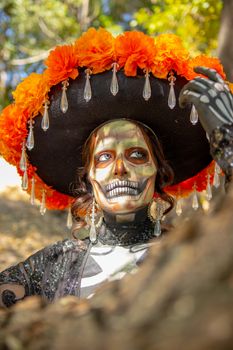 Woman in colorful Day of the Dead skull makeup with floral hat outdoors.