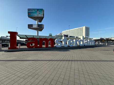 The famous "I amsterdam" sign at Schiphol Airport, framed under a clear blue sky.