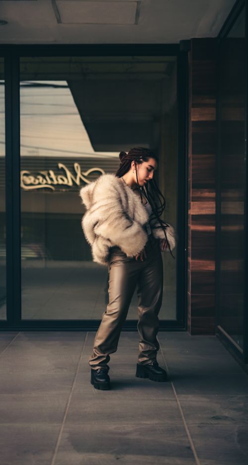 Free Fashionable woman wearing a fur coat standing outside a modern building, exuding a chic and urban vibe. Stock Photo