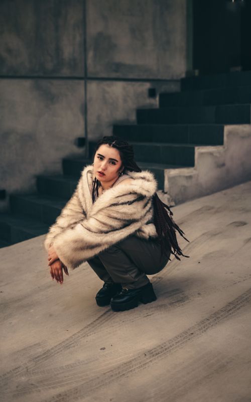 Free Stylish woman in fur coat crouching on a concrete stairway in an urban environment. Stock Photo