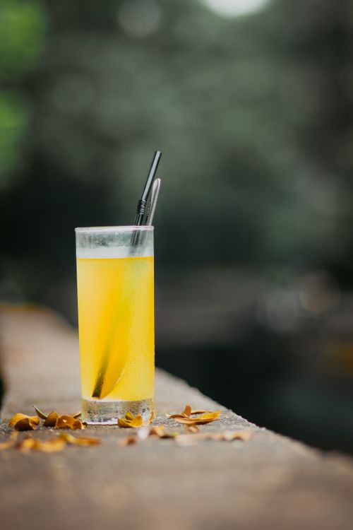 Free Tall glass of citrus juice with straw outdoors, surrounded by autumn leaves. Stock Photo