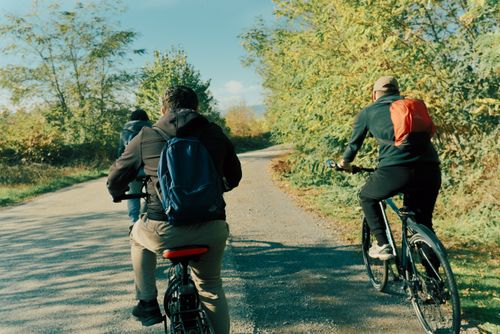 Free Three people biking along a sunlit rural path, surrounded by greenery and a clear blue sky. Stock Photo