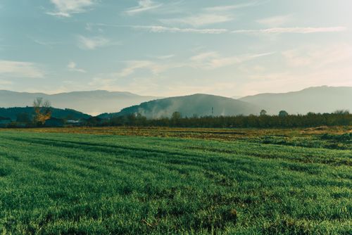Free Picturesque view of a green field with mountains under a blue sky Stock Photo