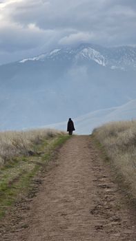 A lone figure walks along a mountain path under cloudy skies in Bakersfield, CA.