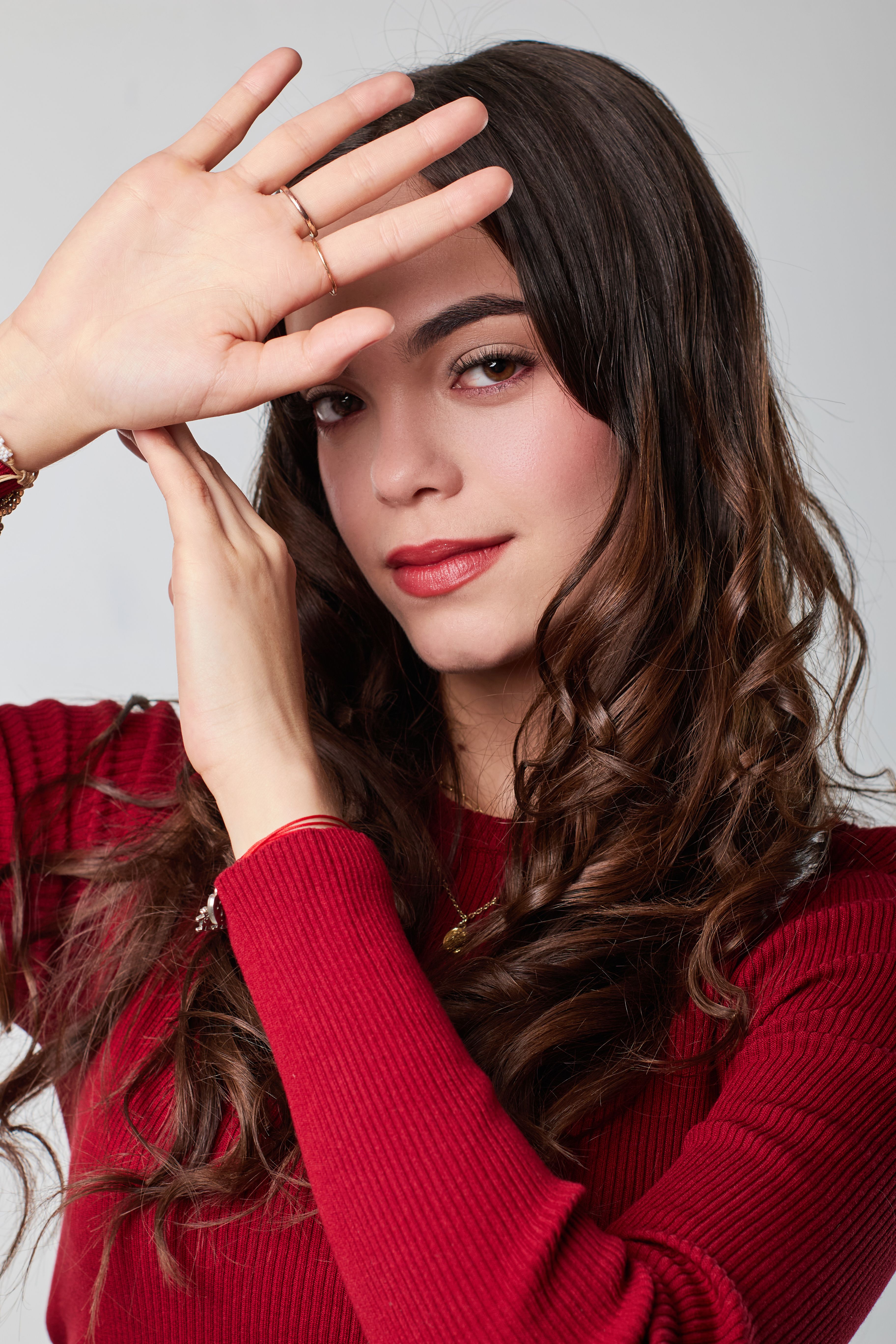 Woman posing with hands framing face in elegant red sweater.
