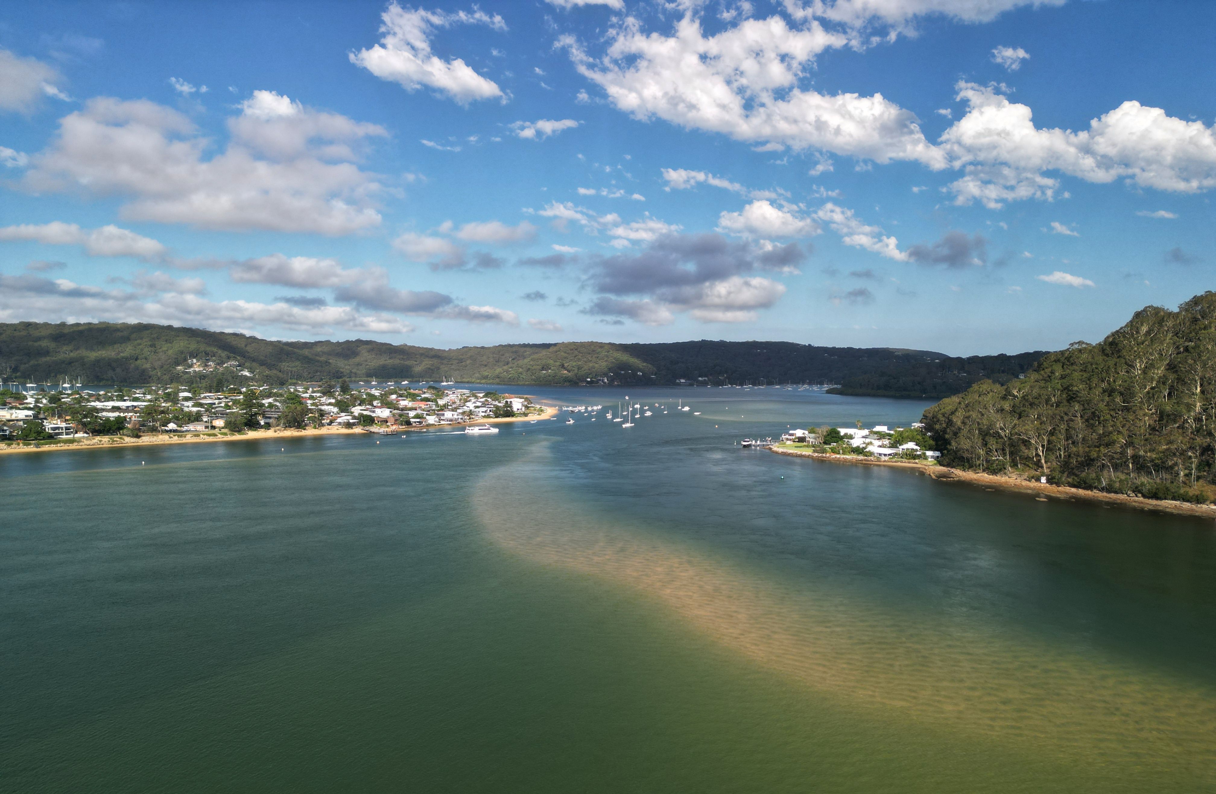 Scenic aerial view of a coastal town by a river with lush green hills and clear skies.