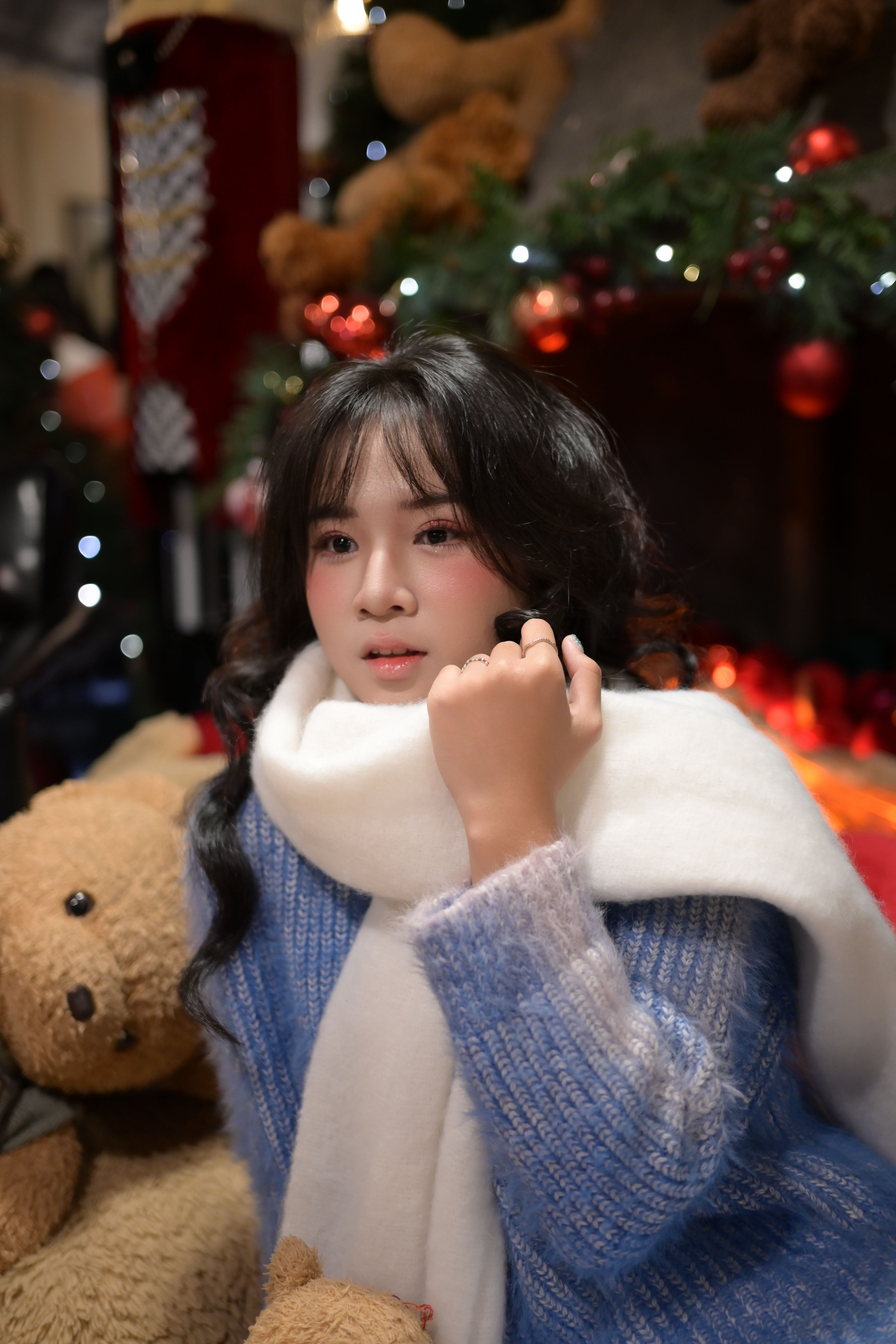 Young woman in a winter setting with a teddy bear by a fireplace.