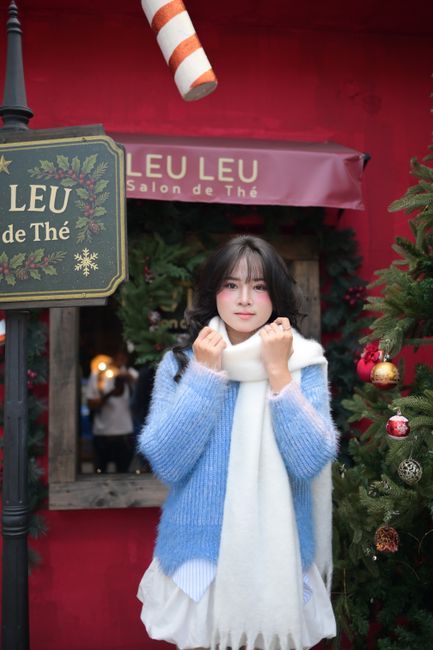Young woman wearing blue sweater and scarf outside decorated cafe during Christmas season.