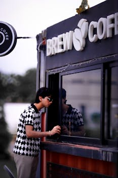 Young man wearing checkered shirt ordering at outdoor coffee kiosk named Brew Coffee.