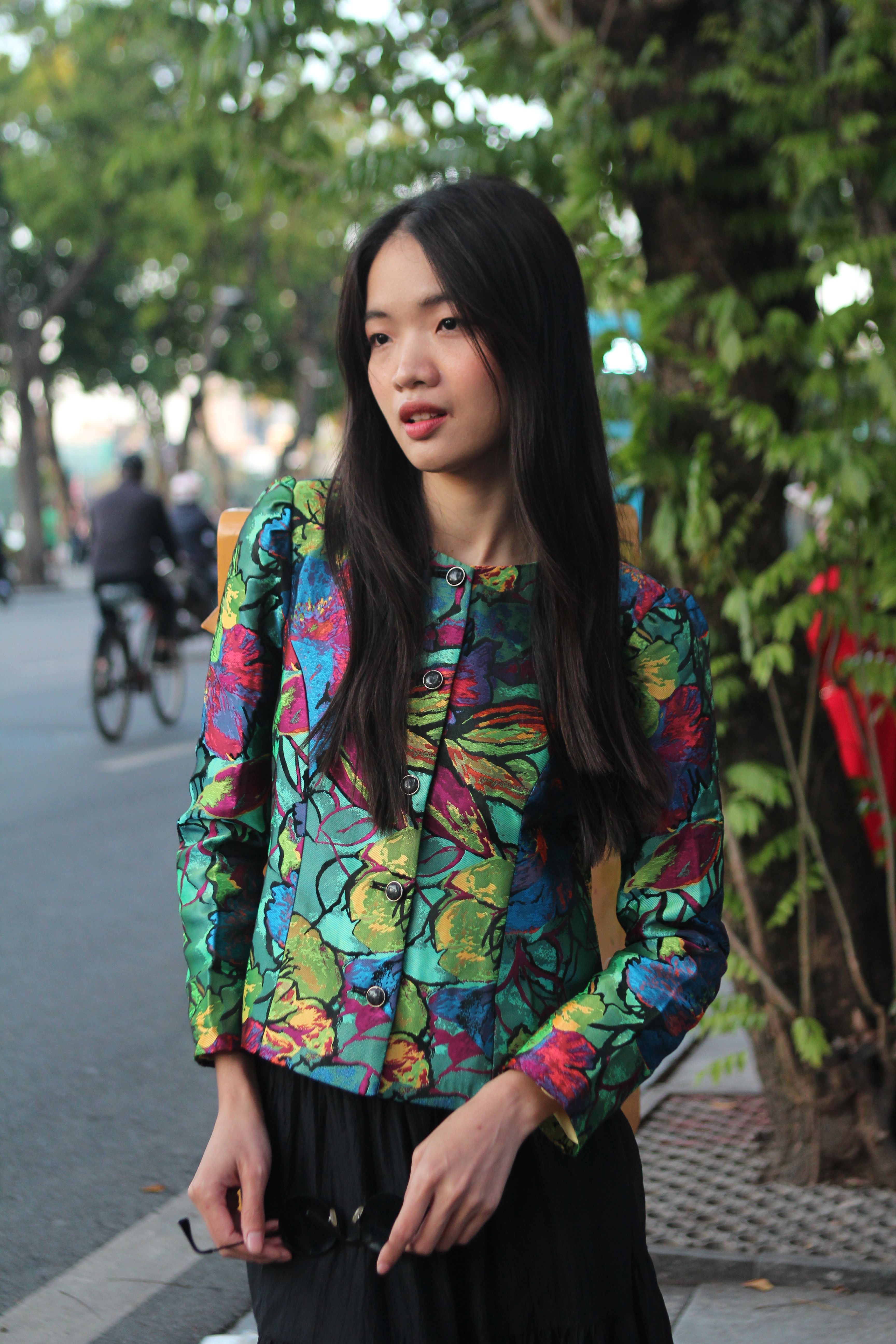 A young woman in a vibrant jacket poses outdoors on a city street.