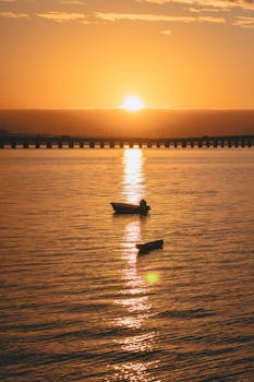 Peaceful sunrise over ocean with boats silhouetted against the golden sky.