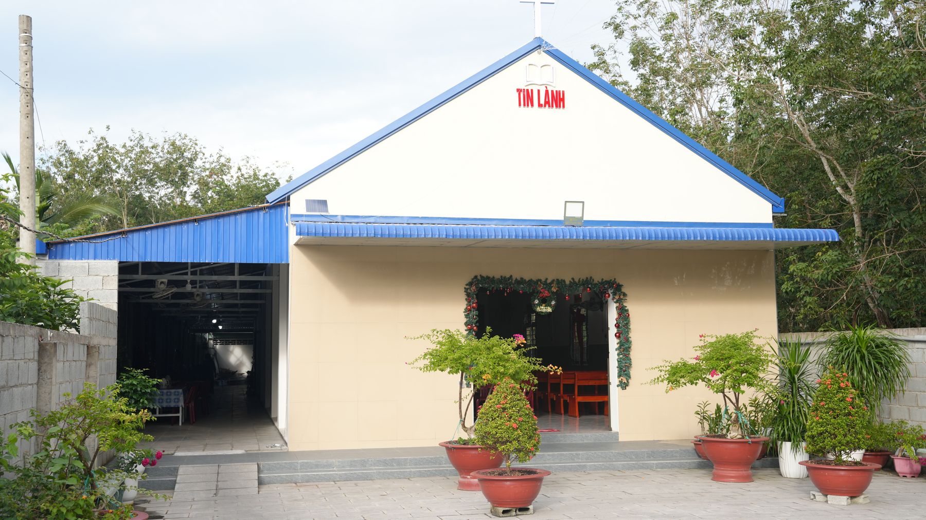 A small rural church with a blue roof, decorated entrance and potted plants.