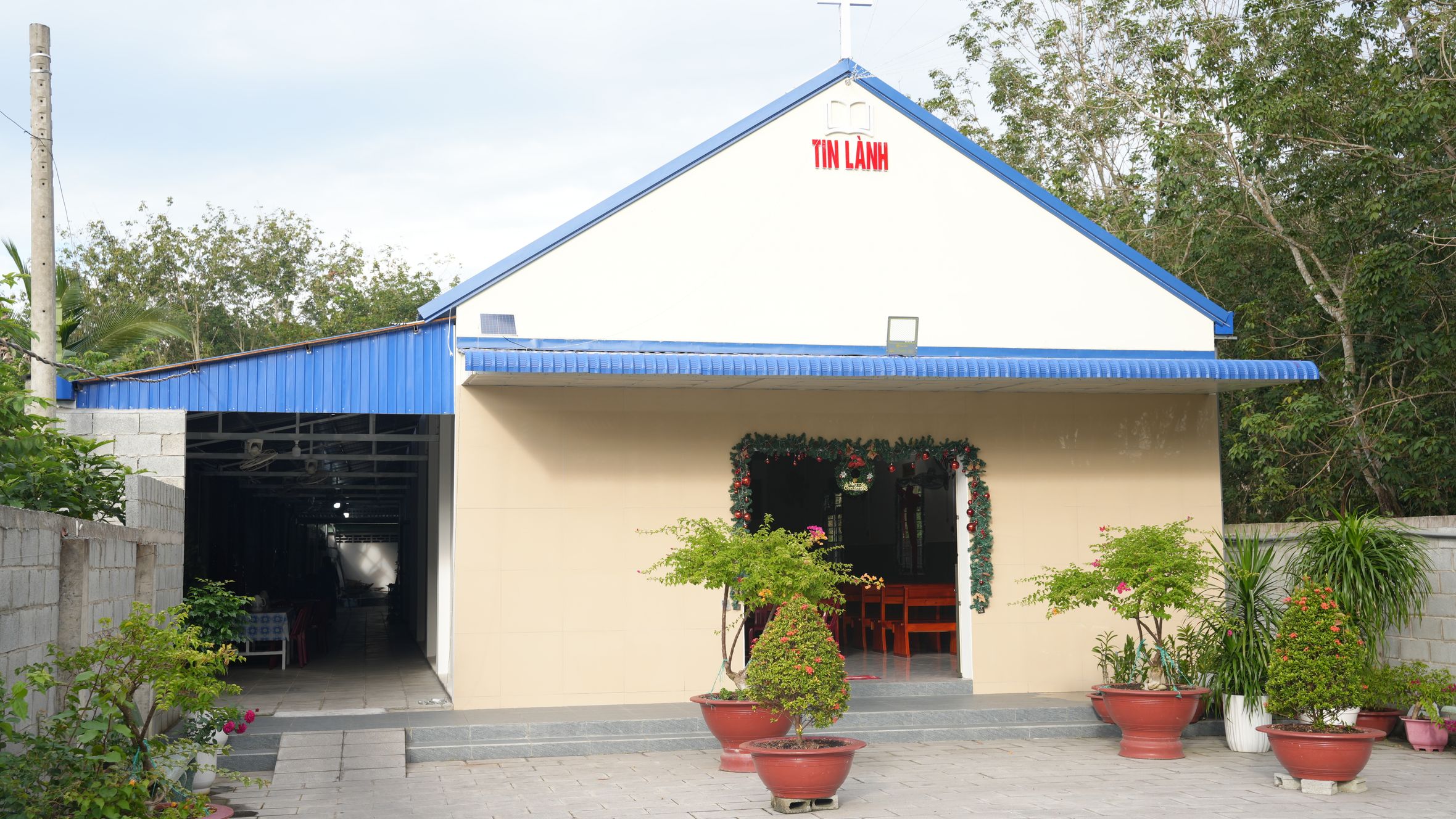 A small rural church with a blue roof, decorated entrance and potted plants.