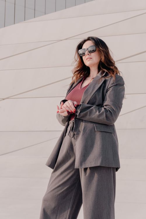 Free A fashionable woman in a gray business suit standing confidently outdoors in sunlight. Stock Photo