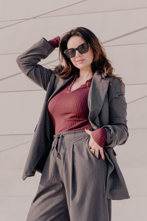 Free Confident woman in sunglasses poses in chic gray suit against modern architecture backdrop. Stock Photo
