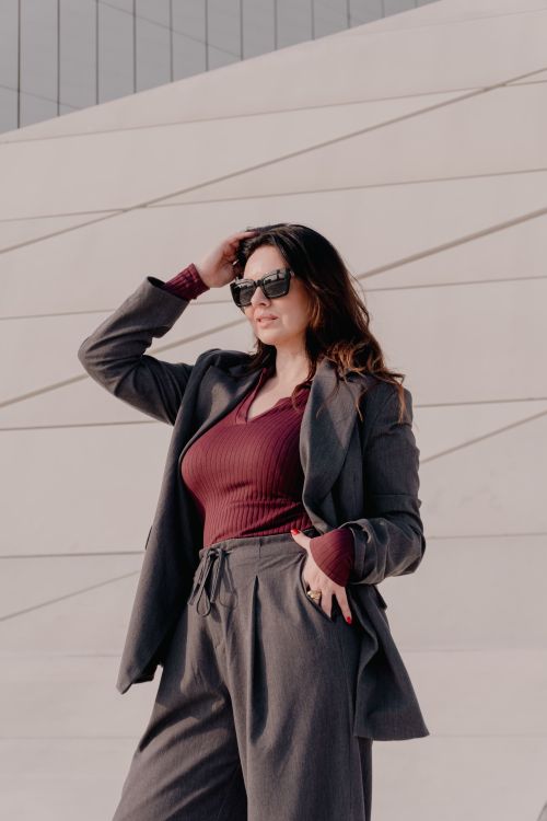 Free Confident woman wearing sunglasses and chic outfit posing against modern architecture. Stock Photo