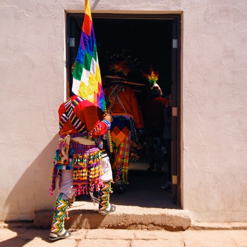 Free Back view of indigenous aborigine of Andes in traditional colorful clothes carrying colorful wiphala flag entering shabby house Stock Photo